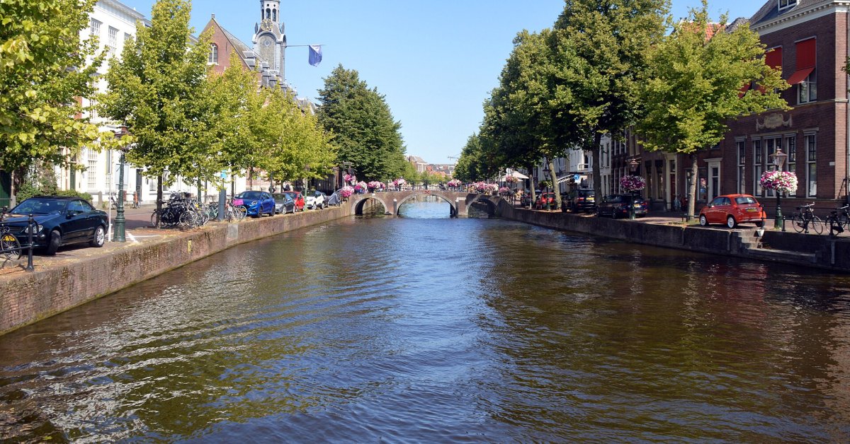 Een gracht in Leiden met een brug, bomen en historische gebouwen langs het water.