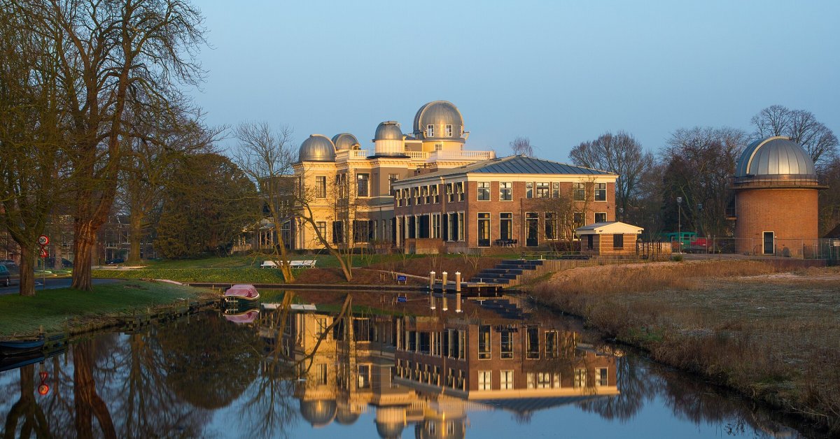 De verlichte historische Sterrewacht in Leiden weerspiegelt in een vijver tussen bomen.