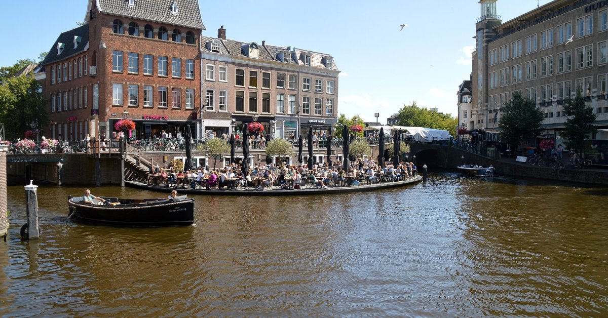 Historische panden en terrassen langs een gracht met een bootje op het water